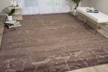 Modern living room with a Nourison Silk Shadows Brown area rug, white bench, orchids, and light wood floors.