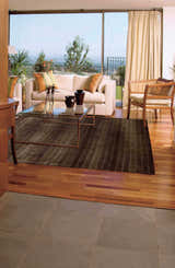 Living room scene with Nourison Aura Chocolate rug, cream sofa, glass coffee table, and view of outdoor landscape.