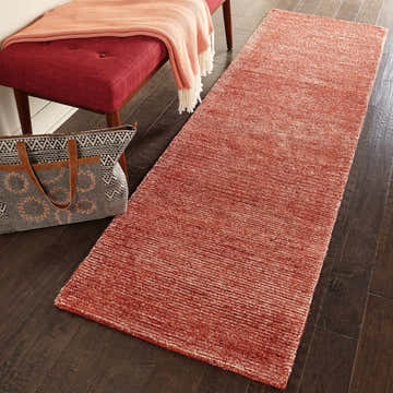 Entryway scene with a Nourison Weston Brick Modern Indoor Area Rug runner, red bench, and patterned tote bag.