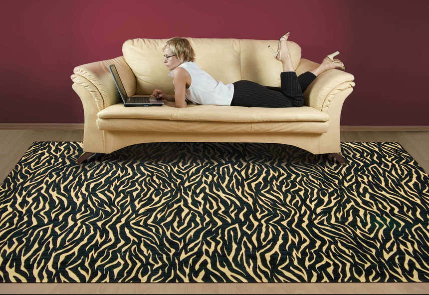 Eclectic living room with a Nourison Cosmopolitan Midnight rug, tan sofa, and a woman working on a laptop.