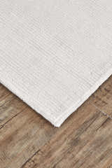 Close up of the textured, hand woven Feizy Batisse Modern Solid White rug on wood floors. Corner