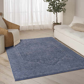 Living room scene with a DKNY Pure Shades Blue Vintage Indoor Area Rug, white sofa, and wicker chair.