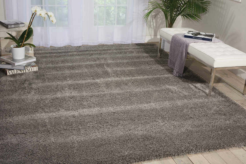 Light-filled room with a Nourison Yummy Shag silver gray rug, white bench, sheer curtains, and wood floors.