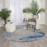 Living room scene with round Nourison Twilight Blue Grey rug, chair, plants, and ottoman.