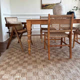 Farmhouse dining room with a beige Ionut Checkered Jute Area Rug under a wood table and woven chairs. Roomscene-Rectangle