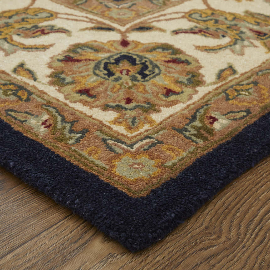 Close up of the Feizy Wagner rug showing its wool texture, navy border, and traditional floral pattern in tan, gold, and blue. Corner