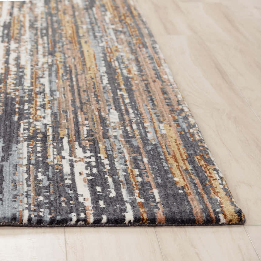 Close-up of Rizzy JAS734 area rug. Abstract design in beige, dark red, gray, ivory, and rust. Machine woven recycled polyester. Corner