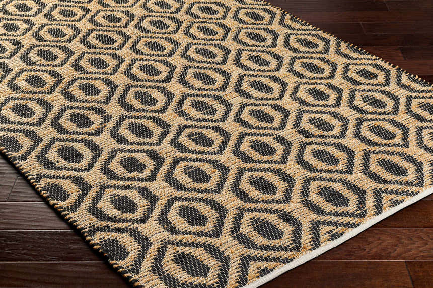 Close-up of the Isaye Charcoal Area Rug showing its jute texture and geometric dark beige and black pattern. Corner