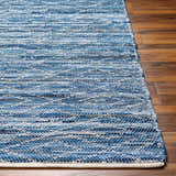 Close-up of the hand-woven Gurit Blue Area Rug. Features stripes in arctic sky, navy, and light gray on a wood floor. Front