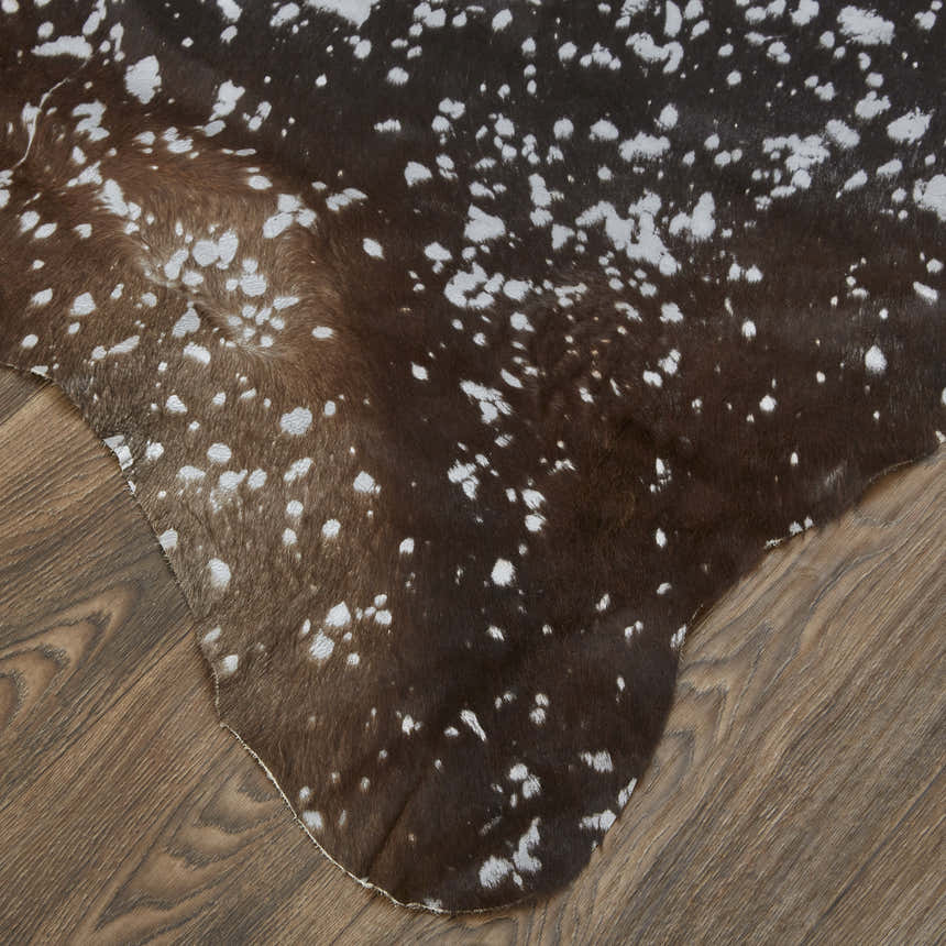 Close-up of Feizy Ellyse rug. Brown cowhide rug with a silver gray animal print pattern on hardwood floor. Corner