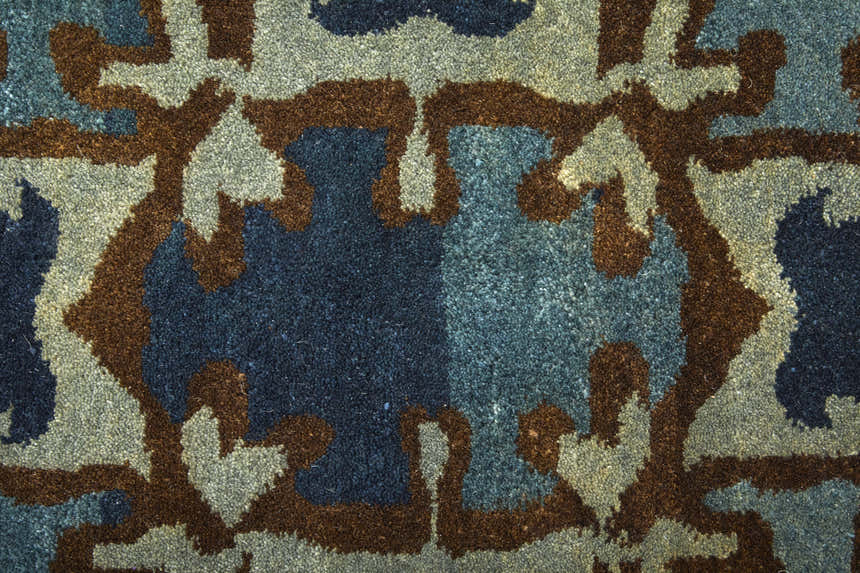 Close-up of the Feizy Amzad Ikat rug, showing a blue, gray, and tan geometric pattern in hand-knotted wool. Texture