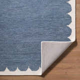 Close-up of the hand-tufted Lukamu Modern Art Deco rug. Blue wool rug with an ivory scalloped edge on hardwood floors. Fold