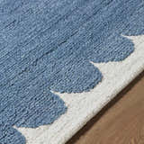 Close up of the blue and ivory Lukamu Modern Art Deco rug, showing its hand-tufted wool texture and scalloped edge. Texture