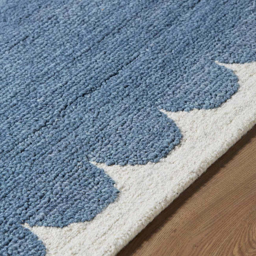 Close up of the blue and ivory Lukamu Modern Art Deco rug, showing its hand-tufted wool texture and scalloped edge. Texture