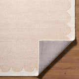 Close-up of a beige Lytufa Modern Art Deco rug showing its wool texture and scalloped ivory edge on a wood floor. Fold