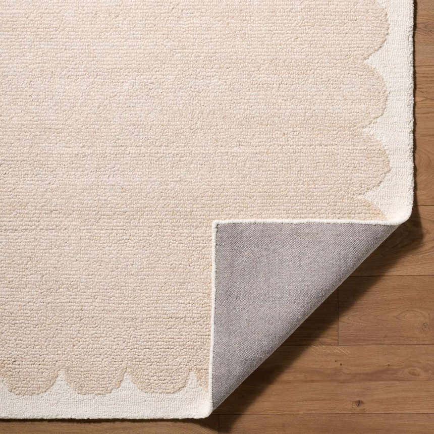 Close-up of a beige Lytufa Modern Art Deco rug showing its wool texture and scalloped ivory edge on a wood floor. Fold