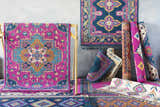 Display of colorful Oban Traditional Rugs in camel, coral, blue, fuchsia, and ivory, rolled and hung against a gray wall. Styleshot