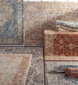 Variety of Morinville rugs in teal, brown, red, and gray with traditional floral patterns, displayed flat and rolled. Styleshot