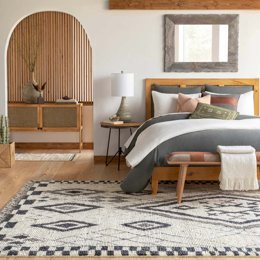 Bedroom scene with a Minyama Area Rug in black, charcoal, cream, and gray, styled with a wood bed, bench, and neutral decor. Roomscene-Rectangle