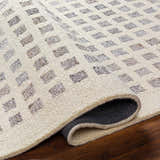 Close-up of the Harib Area Rug showing its beige wool texture and geometric brown and gray square pattern. Fold