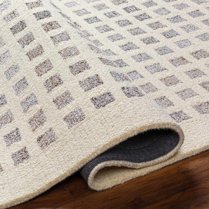 Close-up of the Harib Area Rug showing its beige wool texture and geometric brown and gray square pattern. Fold