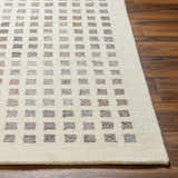 Close-up of the hand-tufted Harib Area Rug. Beige wool rug with a geometric pattern of brown and gray squares. Front