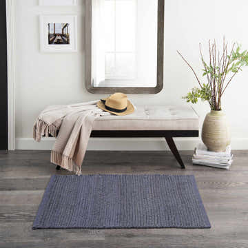 Entryway with a Nourison Natural Jute Navy rug, bench with throw and hat, mirror, vase with greenery. Farmhouse style.