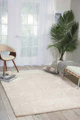 Bright room scene with a Nourison Fantasia Snow Shag rug, white bench, palm tree, and light wood floors.