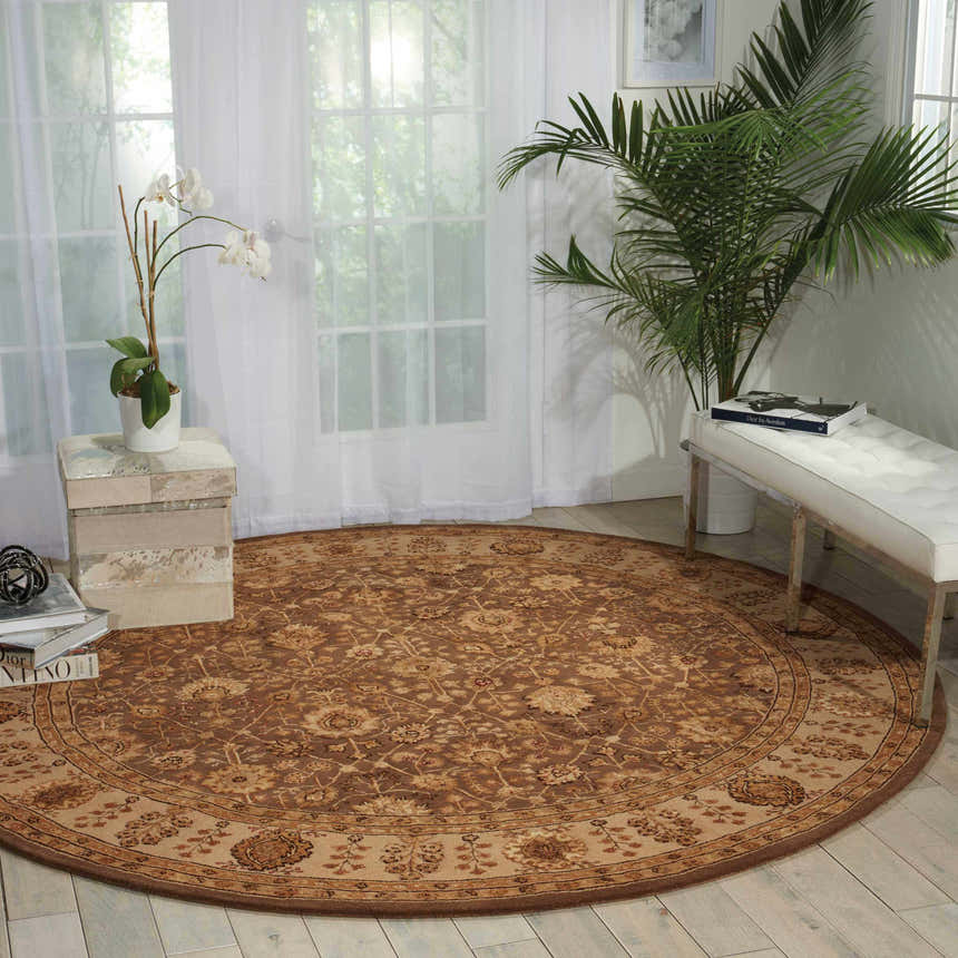 Sunlit room scene with a round Nourison 3000 Taupe Persian rug, white bench, and plants. Airy and bright decor.