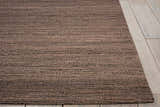 Close-up of the textured, handmade Calvin Klein Monsoon Cinnamon rug in dusty coral on light wood flooring.