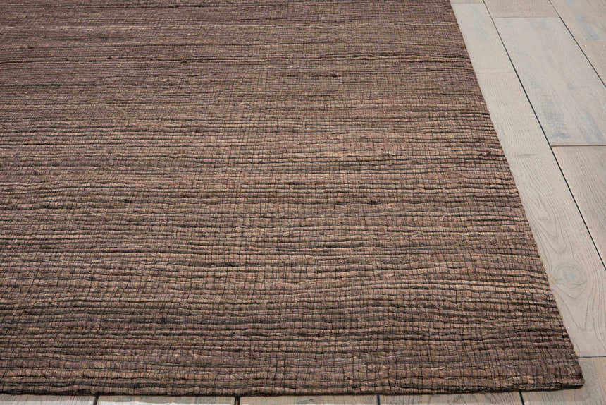 Close-up of the textured, handmade Calvin Klein Monsoon Cinnamon rug in dusty coral on light wood flooring.