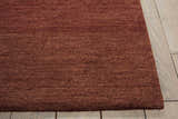 Close-up of the textured Calvin Klein Home Haze Madder rug in madder red on a light wood floor.