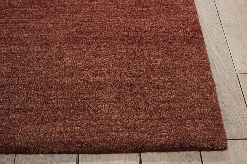 Close-up of the textured Calvin Klein Home Haze Madder rug in madder red on a light wood floor.
