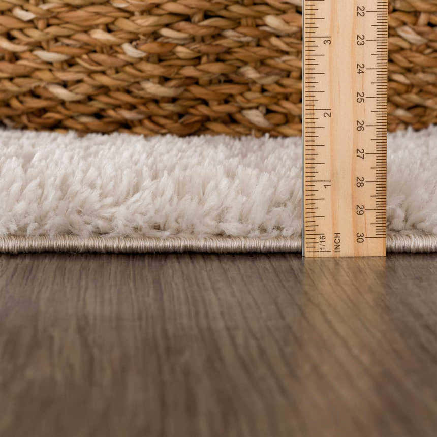 Close-up of the Velora Light Beige rug showing its shag texture, pile height with a ruler, and woven edge. Pile