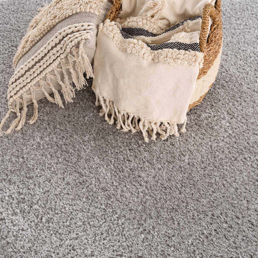 Close-up of the gray Lunaro rug texture with a basket, pillow, and throw blanket. Modern, minimalist style. Swatch