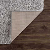 Close-up of the Lunaro Gray shag rug showing texture, backing, and edge on dark wood floor. Fold