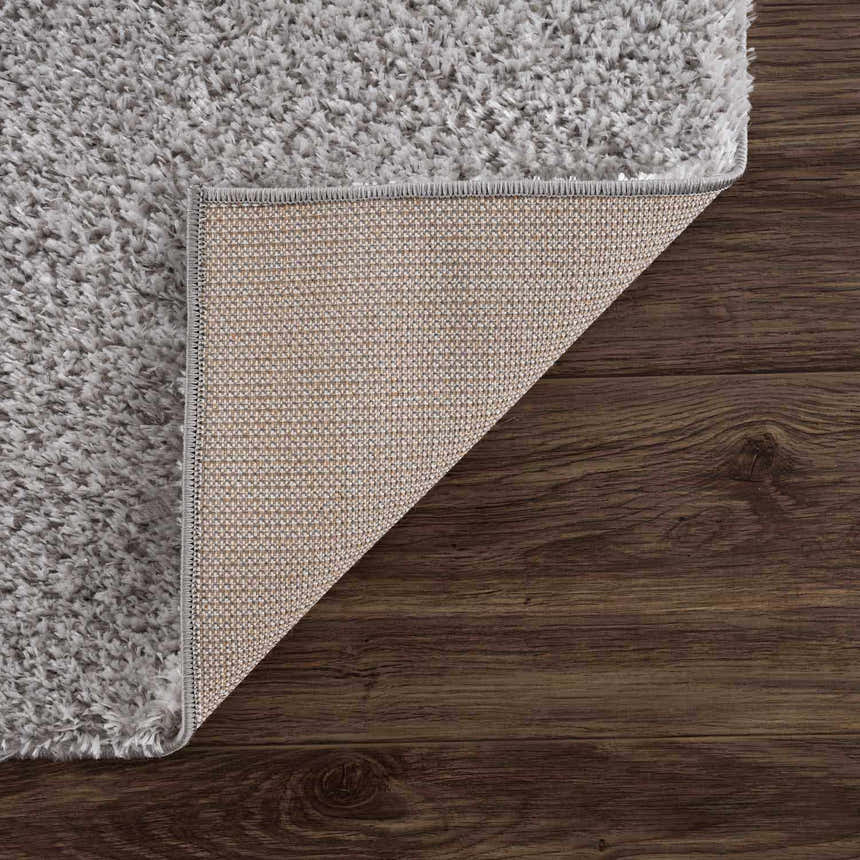 Close-up of the Lunaro Gray shag rug showing texture, backing, and edge on dark wood floor. Fold