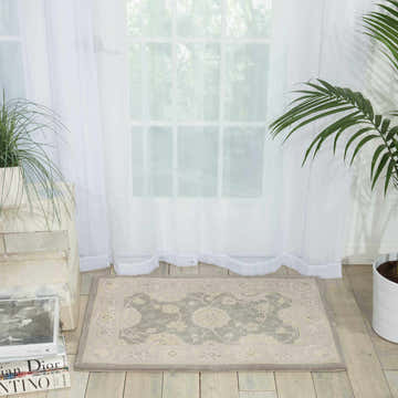 Light-filled room with a taupe Nourison 2000 Slate Persian rug, plants, books, and sheer white curtains.
