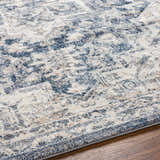 Close up of the Shotts Thick Luxe Rug, showing its traditional pattern in cream, tan, and dark blue on wood flooring. Texture