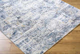 Close-up of the Hyman Area Rug, a contemporary rug with a pattern in camel, gray, and denim on a wood floor. Corner