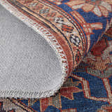 Close-up of Feizy Rawlins rug showing intricate geometric medallion pattern in red, tan, and blue with gray backing. Fold