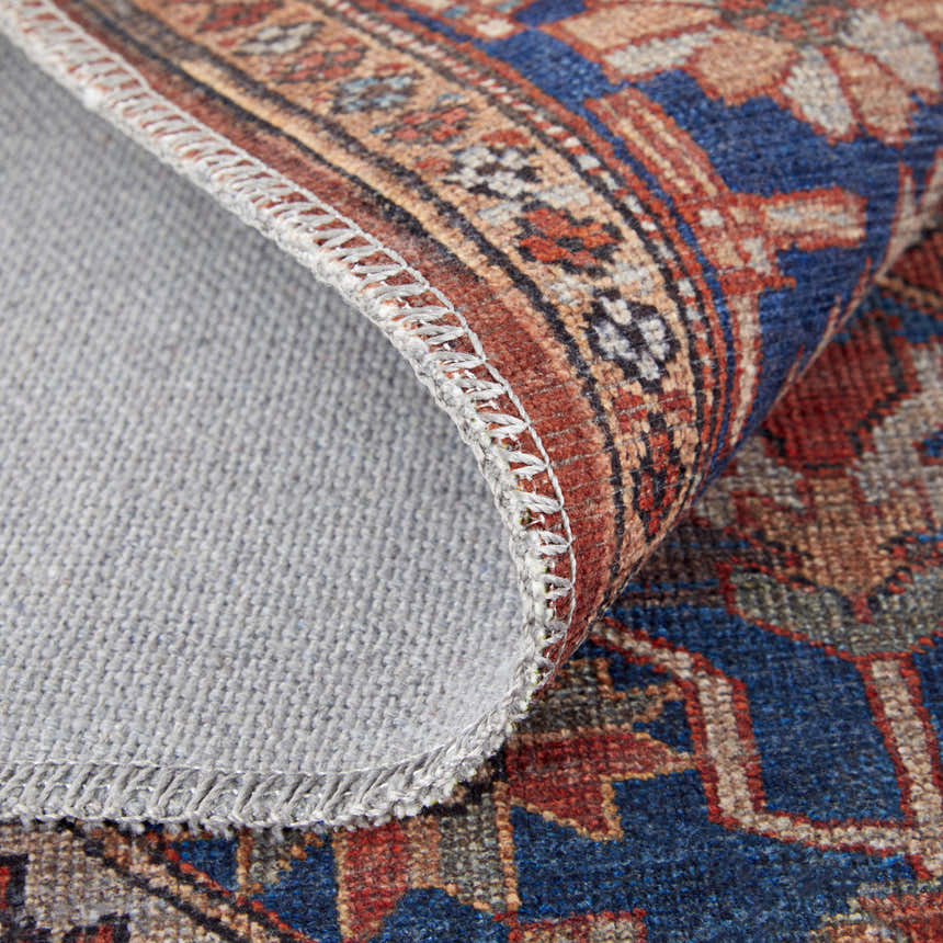 Close-up of Feizy Rawlins rug showing intricate geometric medallion pattern in red, tan, and blue with gray backing. Fold