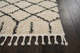Close up of Nourison Moroccan Shag Cream Tribal rug showing shag texture, diamond pattern, and fringe detail on dark wood floor.