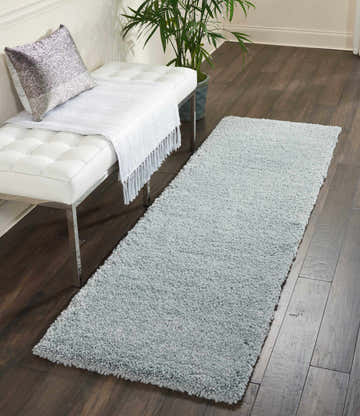 Entryway scene with a Nourison Malibu Shag Slate rug, white bench, silver pillow, and dark wood floors.