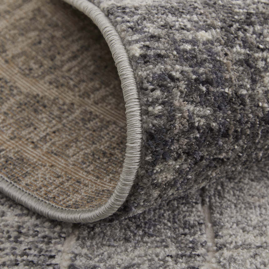 Close-up of the Feizy Kano rug showing its abstract black, gray, and ivory pattern and textured jute and polyester fibers. Fold