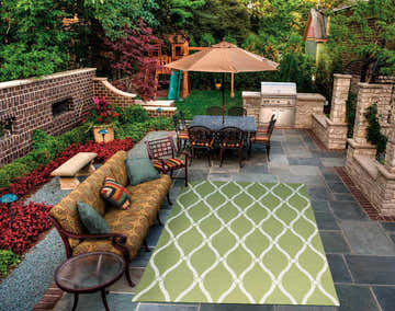 Outdoor patio scene with green Nourison Home & Garden area rug, sofa, dining table, and grill.