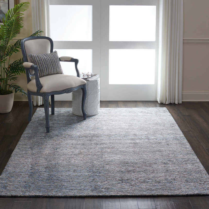 Living room scene with taupe Nourison Ellora Slate rug, blue accent chair, white garden stool, and dark wood floors.