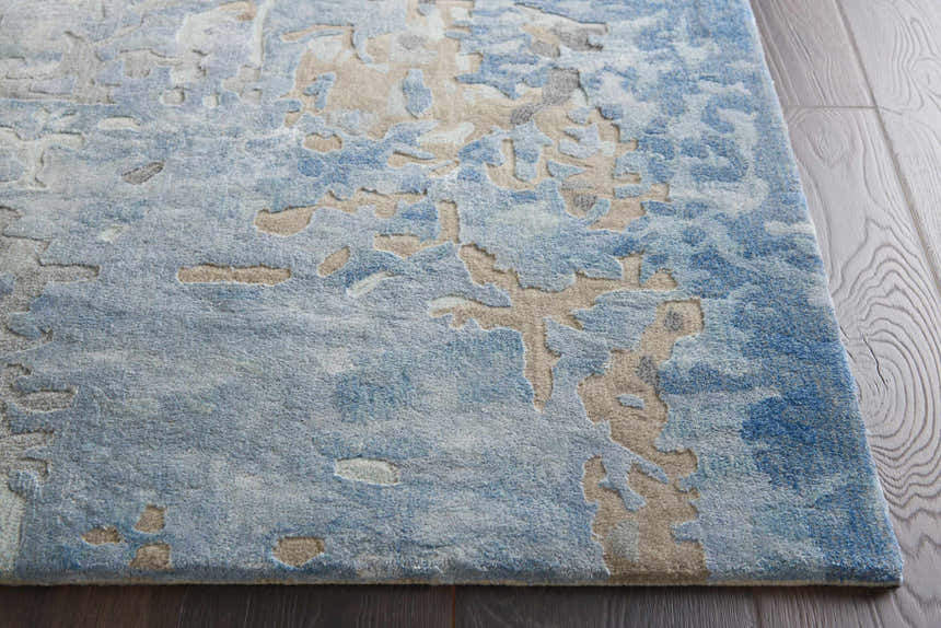 Close up of the Nourison Prismatic Denim rug showing its abstract pattern, texture, and colors on a dark wood floor.