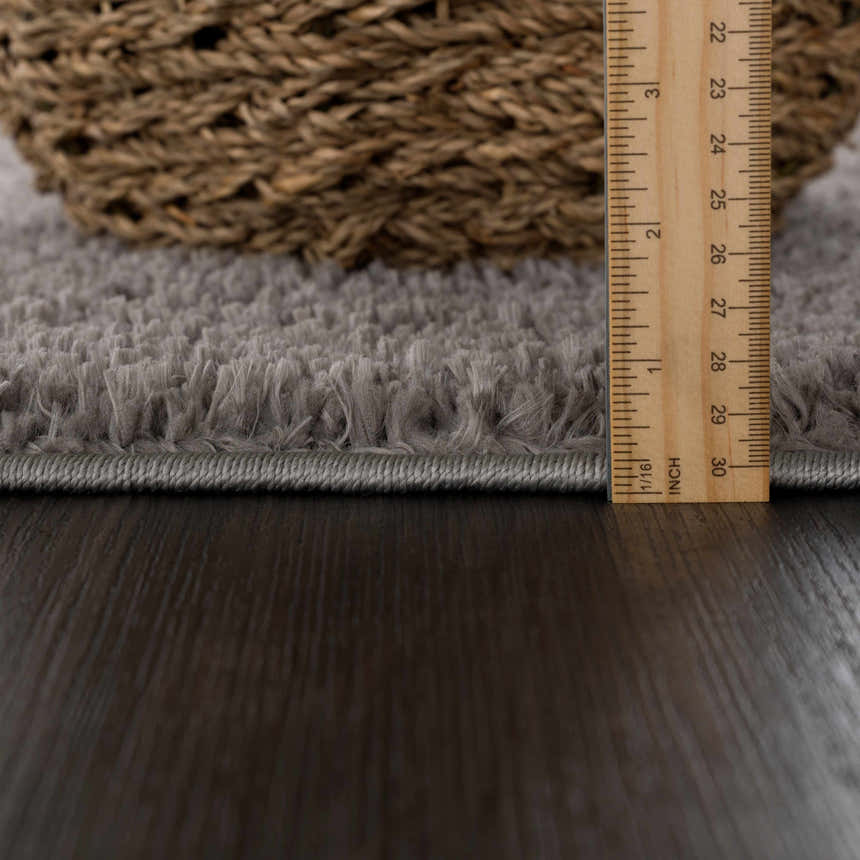 Close-up of the Judy Solid Dark Gray Washable Shag Rug showing its plush texture and pile height with a ruler. Pile
