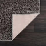 Close-up of the Judy Solid Dark Gray Washable Shag Rug showing its plush texture and non-slip backing on dark wood floor. Fold
